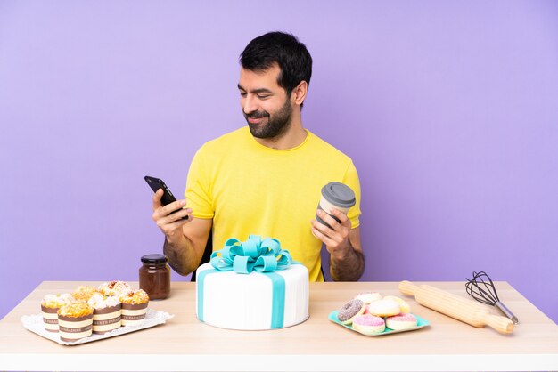 Hombre en una mesa con un gran pastel con café para llevar y un móvil