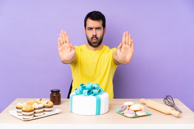 Hombre en una mesa con un gran pastel haciendo gesto de parada y decepcionado