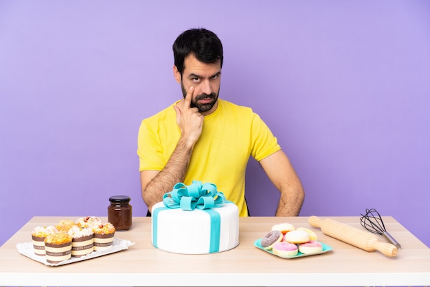 Hombre en una mesa con un gran pastel mostrando algo