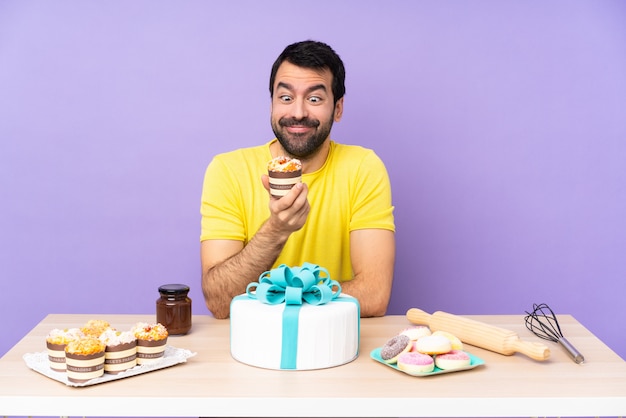 Foto hombre en una mesa con un gran pastel sobre fondo morado