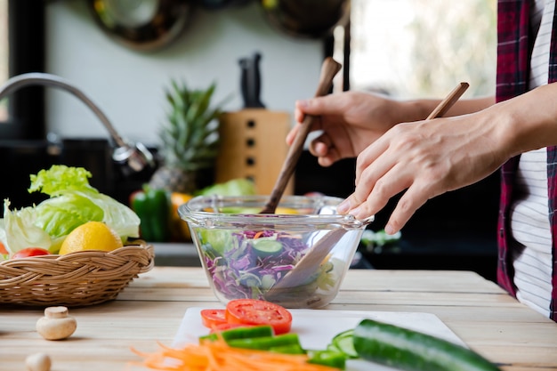 Hombre mezclando verduras frescas en un tazón mientras está de pie en la cocina haciendo ensalada.