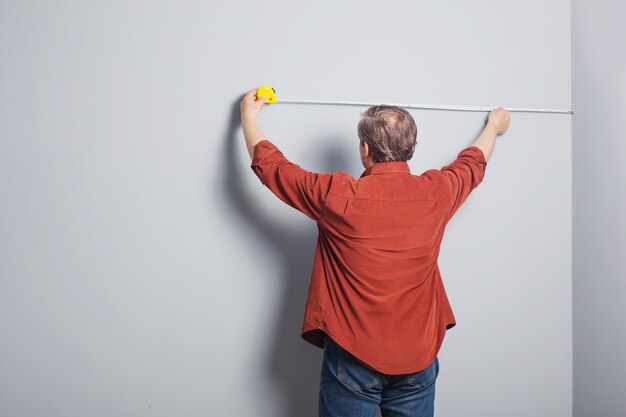 El hombre mide una pared gris con cinta de construcción