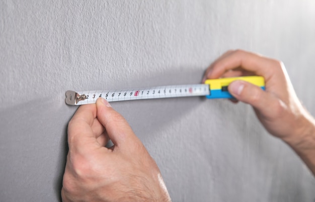 El hombre mide una pared gris con cinta métrica.