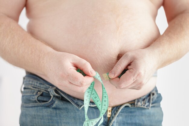 Hombre midiendo su barriga gorda con cinta métrica