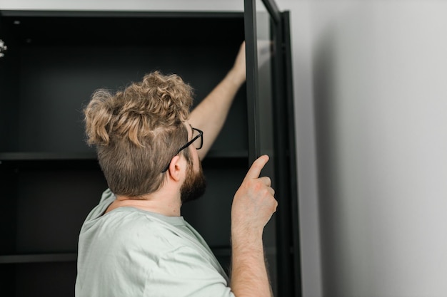 Hombre milenario barbudo monta su estantería Utiliza herramientas para muebles Muebles para la habitación interior o apartamentos