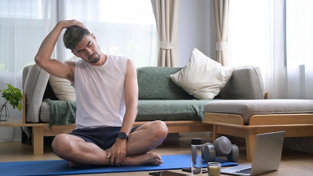 Hombre milenario haciendo ejercicio en casa y viendo lecciones de fitness en línea en una laptop