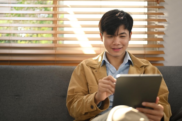 Un hombre milenario relajado que trabaja en línea o revisa la aplicación social en una tableta digital mientras está sentado en la sala de estar