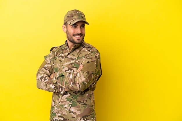 Hombre militar aislado sobre fondo amarillo con los brazos cruzados y feliz