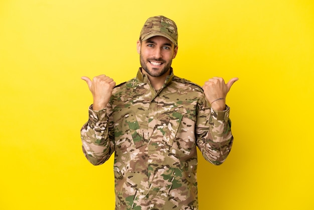 Hombre militar aislado sobre fondo amarillo con gesto de pulgar hacia arriba y sonriente