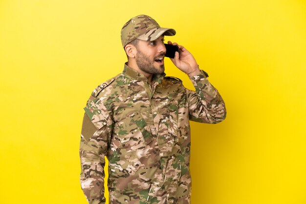 Hombre militar aislado sobre fondo amarillo manteniendo una conversación con el teléfono móvil