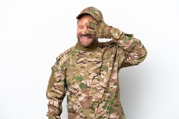 Hombre militar aislado sobre fondo blanco que cubre los ojos con las manos y sonriendo