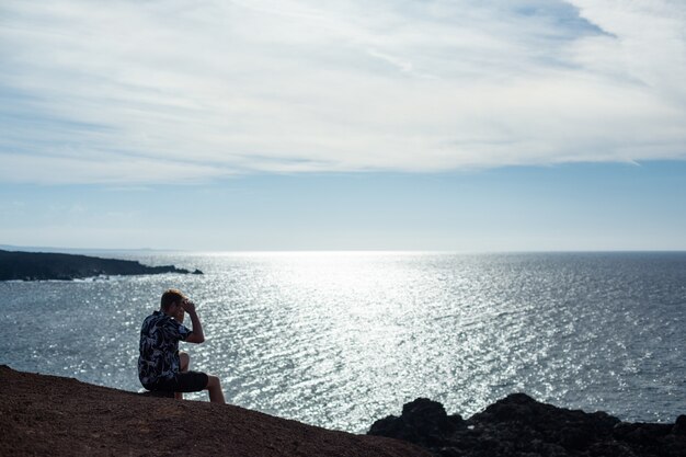 Un hombre mira al mar, sentado sobre una piedra. La famosa playa de El Golfo, Lanzarote.