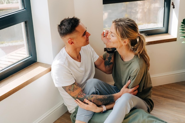 Foto un hombre mira con amor a su mujer una pareja enamorada se sienta juntos en el suelo de la sala de estar