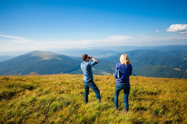 El hombre mira con binoculares mirando las montañas de los Cárpatos y la mujer a su lado.