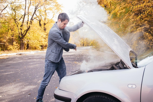 Un hombre mira debajo del capó abierto de un automóvil El automóvil se descompuso en la carretera El motor echa humo