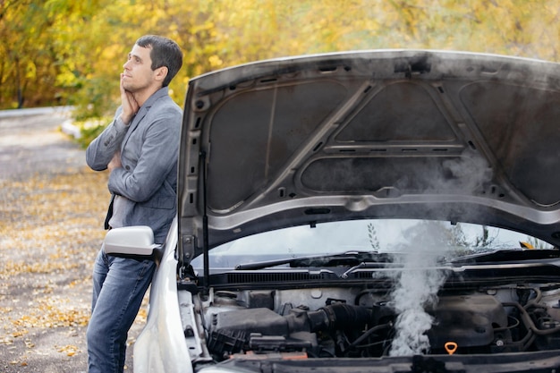 Un hombre mira debajo del capó abierto de un automóvil El automóvil se descompuso en la carretera El motor echa humo