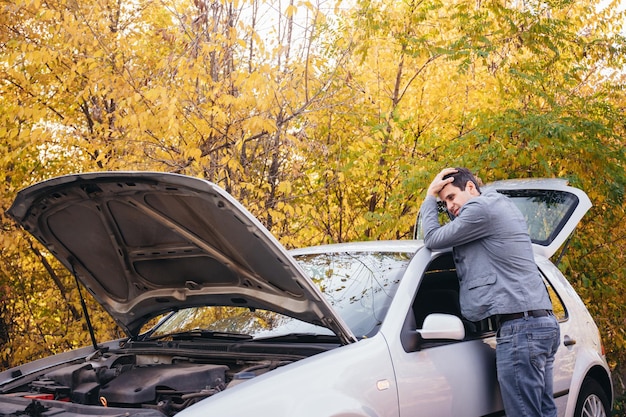Foto un hombre mira debajo del capó abierto de un automóvil el automóvil se descompuso en la carretera