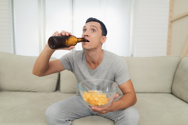 Un hombre mira con entusiasmo la televisión y bebe cerveza.