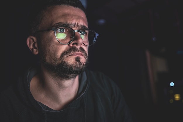 Un hombre mira fijamente a la pantalla de una computadora en la oscuridad por la noche, copie el espacio.