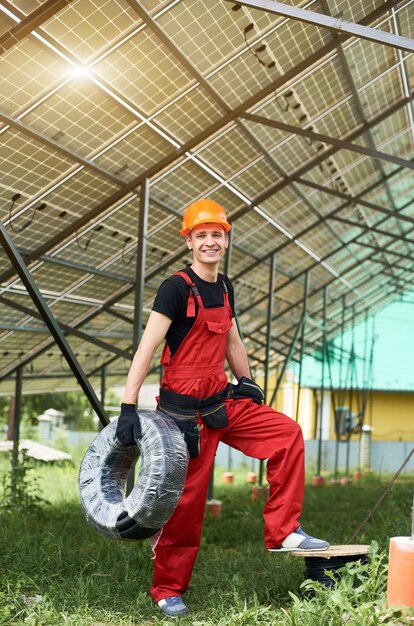 El hombre mira los paneles solares con una bobina de cables en sus manos en un terreno cerca de la casa