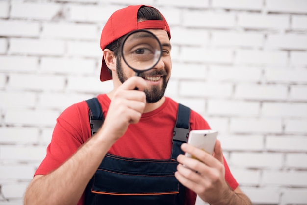 El hombre mira a través de la lupa arregla el teléfono inteligente.