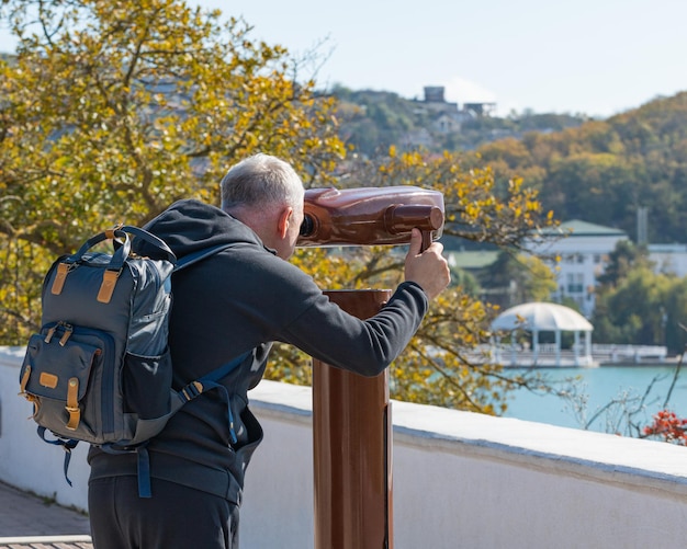 Un hombre mira a través de un telescopio turístico en el paisaje otoñal del lago y las montañas