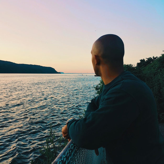 Hombre mirando al mar contra un cielo despejado durante la puesta de sol