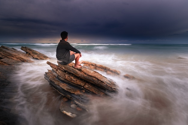 Hombre mirando al mar mientras el mar golpea las rocas en Bidart, País Vasco.