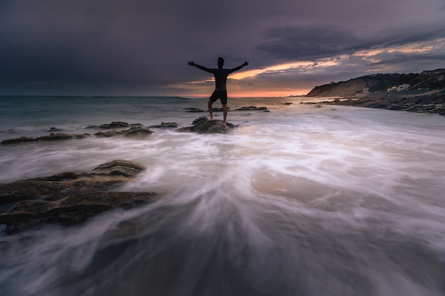 Foto hombre mirando al mar mientras el mar golpea las rocas en bidart, país vasco.