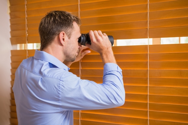 Hombre mirando con binoculares a través de las persianas