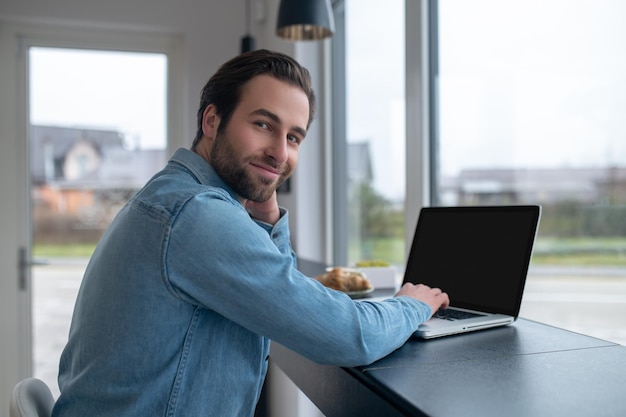 Hombre mirando a la cámara sentado en la computadora portátil en el café