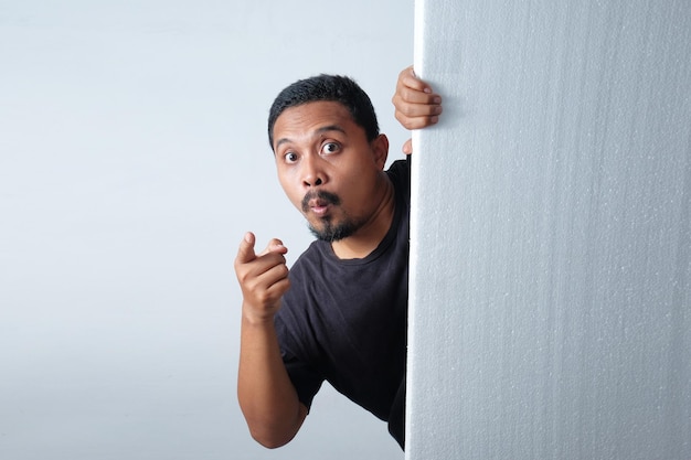 Hombre mirando detrás de la pared mientras señala con el dedo