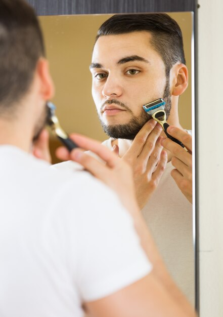 Hombre mirando el espejo y la cara afeitado con maquinilla de afeitar