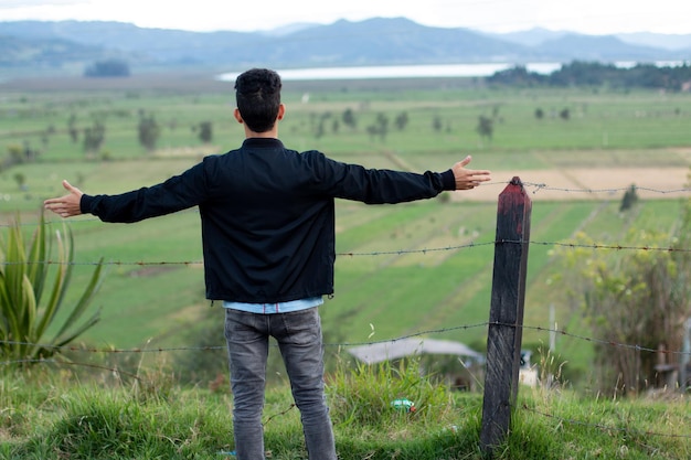 Hombre mirando hermosos paisajes con prados, montañas y un lago de fuquene.