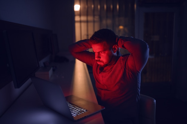 Hombre mirando portátil y sentado en la oficina a altas horas de la noche.