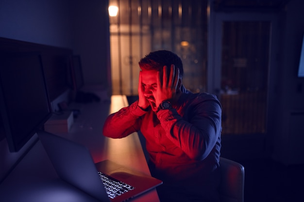 Hombre mirando portátil y sentado en la oficina a altas horas de la noche.