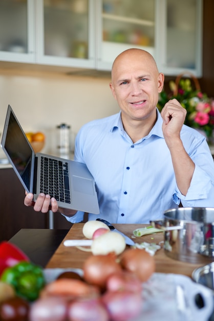 Hombre mirando la receta en la computadora portátil mientras se cocina la cena