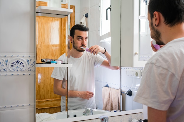 Hombre mirando a sí mismo en un espejo en el baño. El esta cepillando sus dientes