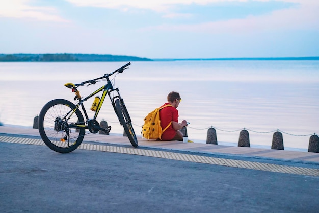 Hombre con mochila amarilla sentado solo junto al lago en la ciudad Viajando en bicicleta