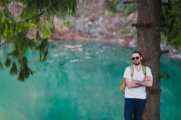 Hombre con mochila descansando contra un árbol junto a un lago