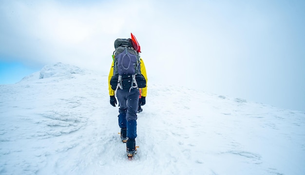 Hombre con mochila grande caminando hasta la cima de la montaña nevada de invierno