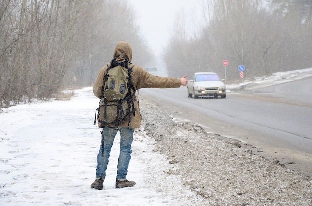 Un hombre con una mochila grande que muestra los pulgares para hacer autostop.