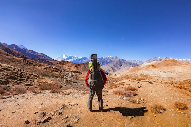 Un hombre con una mochila y una guitarra se para y mira románticamente las montañas de Nepal. Vista trasera.