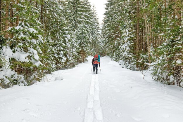 Hombre con mochila en nieve profunda al bosque de invierno