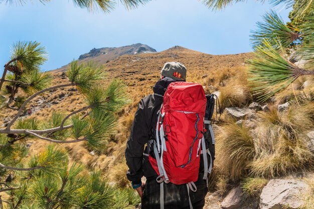 Foto hombre con mochila observa la cima de una montaña que simboliza la motivación y el logro de la meta