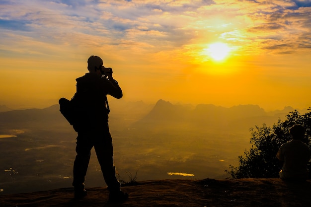 Hombre mochilero con su silueta de cámara réflex digital en el fondo del atardecer