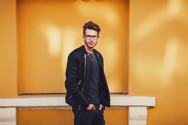 Hombre de moda en la chaqueta de cuero que presenta cerca de la pared coloreada