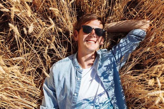 Hombre de moda con gafas de sol en el campo de trigo