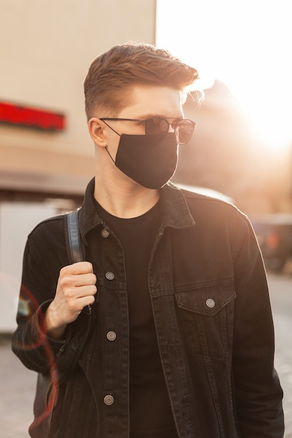 Hombre de moda joven guapo con gafas de sol con mochila y vistiendo una máscara de contaminación facial