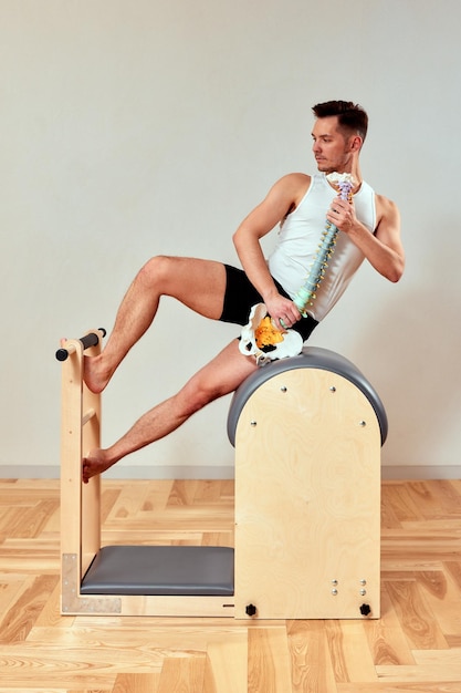 Un hombre con un modelo de la columna vertebral en sus manos durante el pilates en el reformador un joven muestra cómo